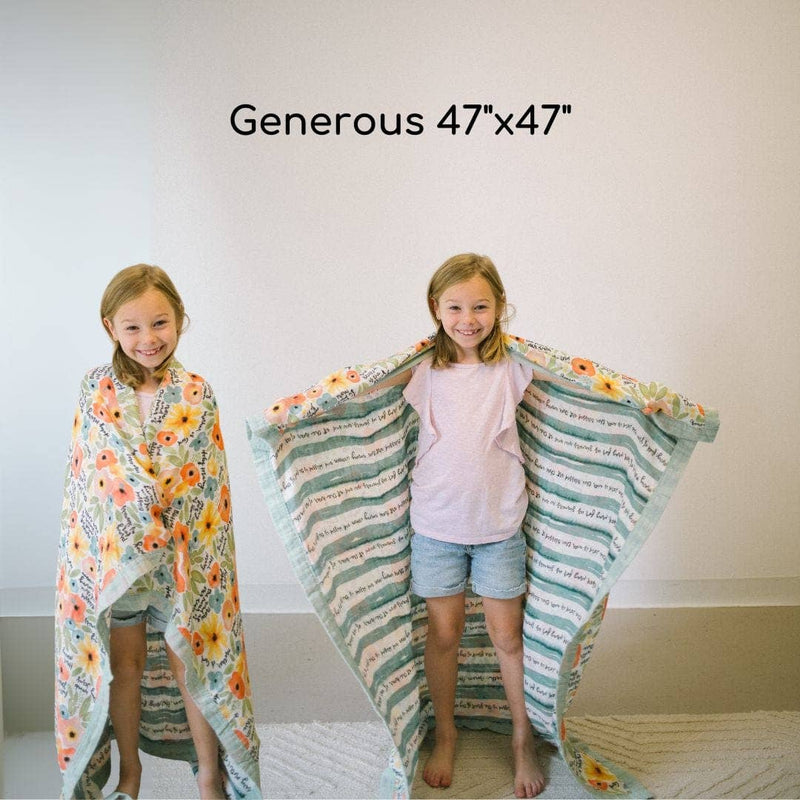 Two children holding a large floral blanket with text, standing on a white floor.