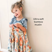 Child holding a floral ultra-soft bamboo muslin blanket against a light background
