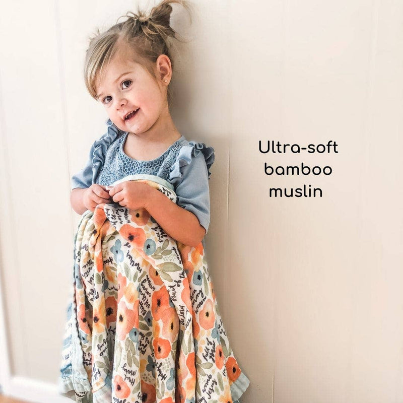 Child holding a floral ultra-soft bamboo muslin blanket against a light background