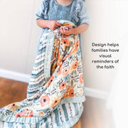 Child holding a floral-patterned blanket with text, standing against a plain background.